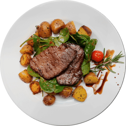 Plato de carne asada jugosa acompañada de papas doradas, espinacas frescas y un tomate cherry, decorado con ramitas de romero. Ideal para una comida nutritiva y deliciosa.