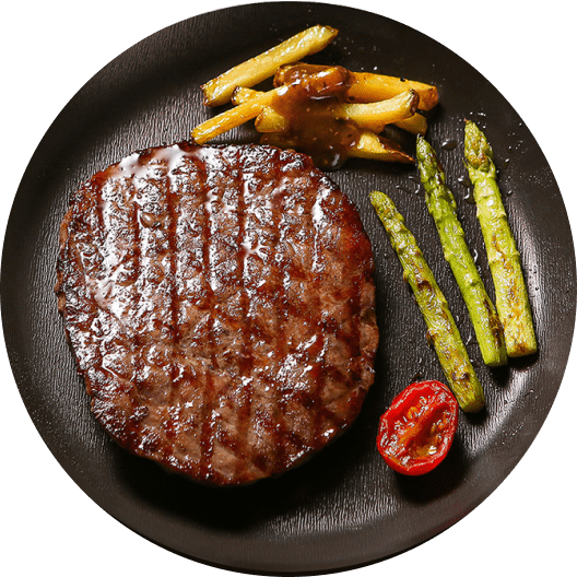 Plato de carne asada jugosa acompañada de papas fritas y espárragos verdes, servido en un plato negro.