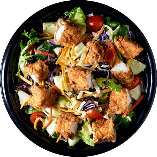 Ensalada fresca con lechuga, tomates cherry, pollo frito, queso rallado y aderezo, presentada en un plato negro. Ideal para una comida saludable y sabrosa.
