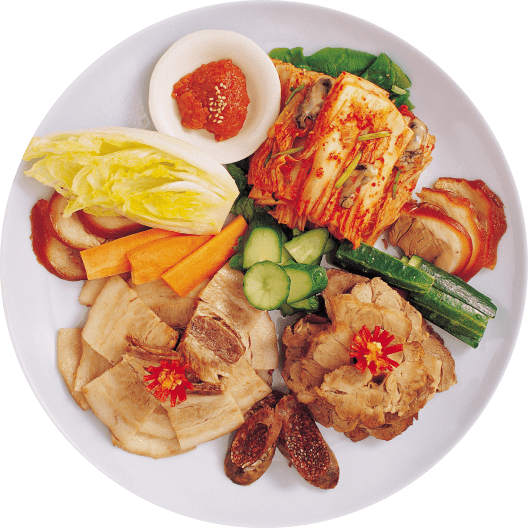 Plato de comida asiática con variedad de vegetales frescos, kimchi, y diferentes tipos de carne, decorado con flores comestibles y salsas.